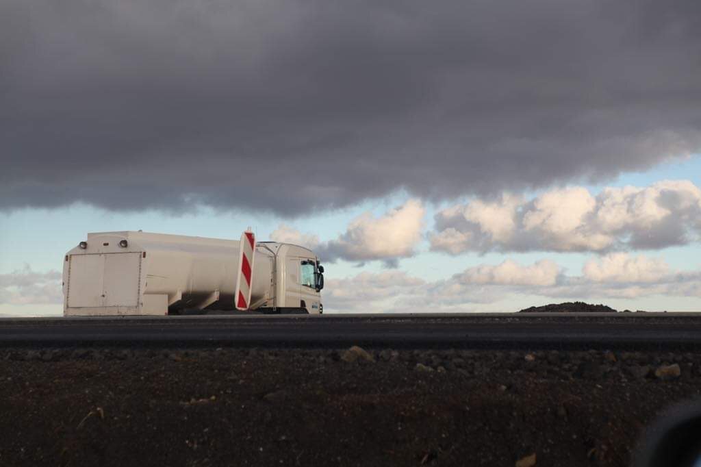 Hvítur tankbíll við nýlagðan veg undir þungbúnum himni.