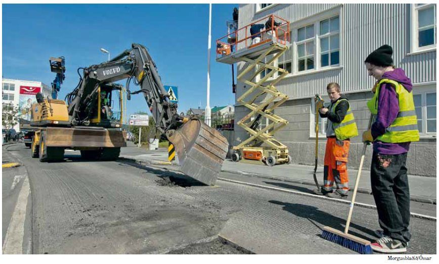 Grafa á vörubílspalli og starfsmenn Loftorku með kústa við gatnaviðgerð.